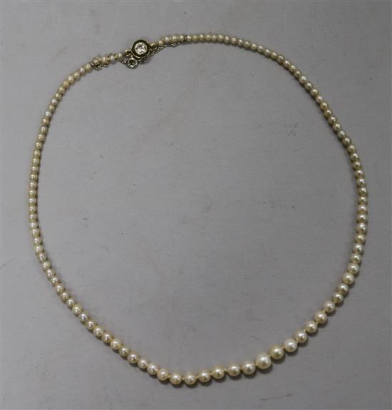 A graduated row of cultured pearls with an emerald and diamond set clasp, 19cm drop